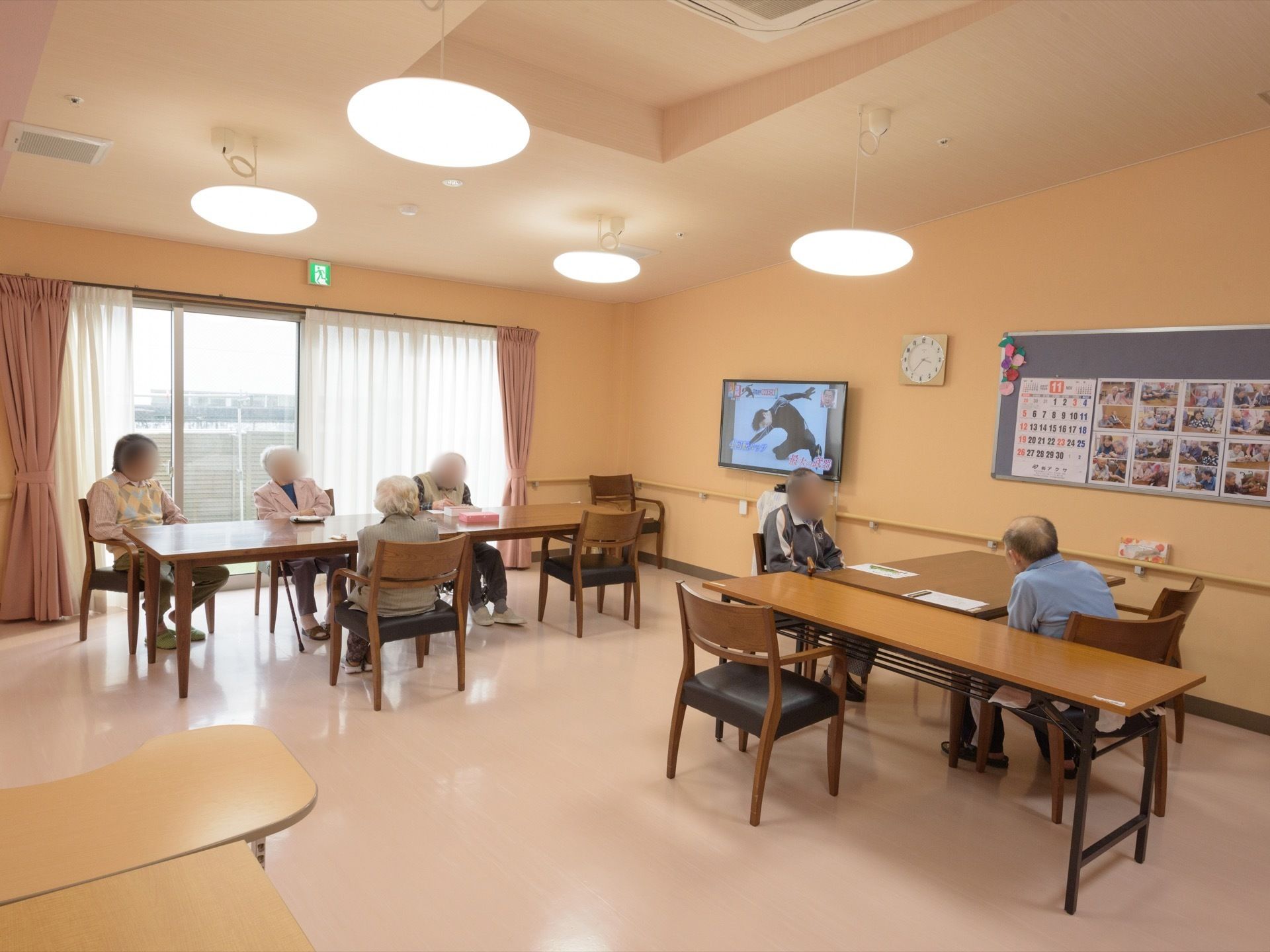 窓があり明るく開放的な室内である。入居者様がテレビを鑑賞をしたり、制作活動を行ったりしている。壁には手すりが備わっている。