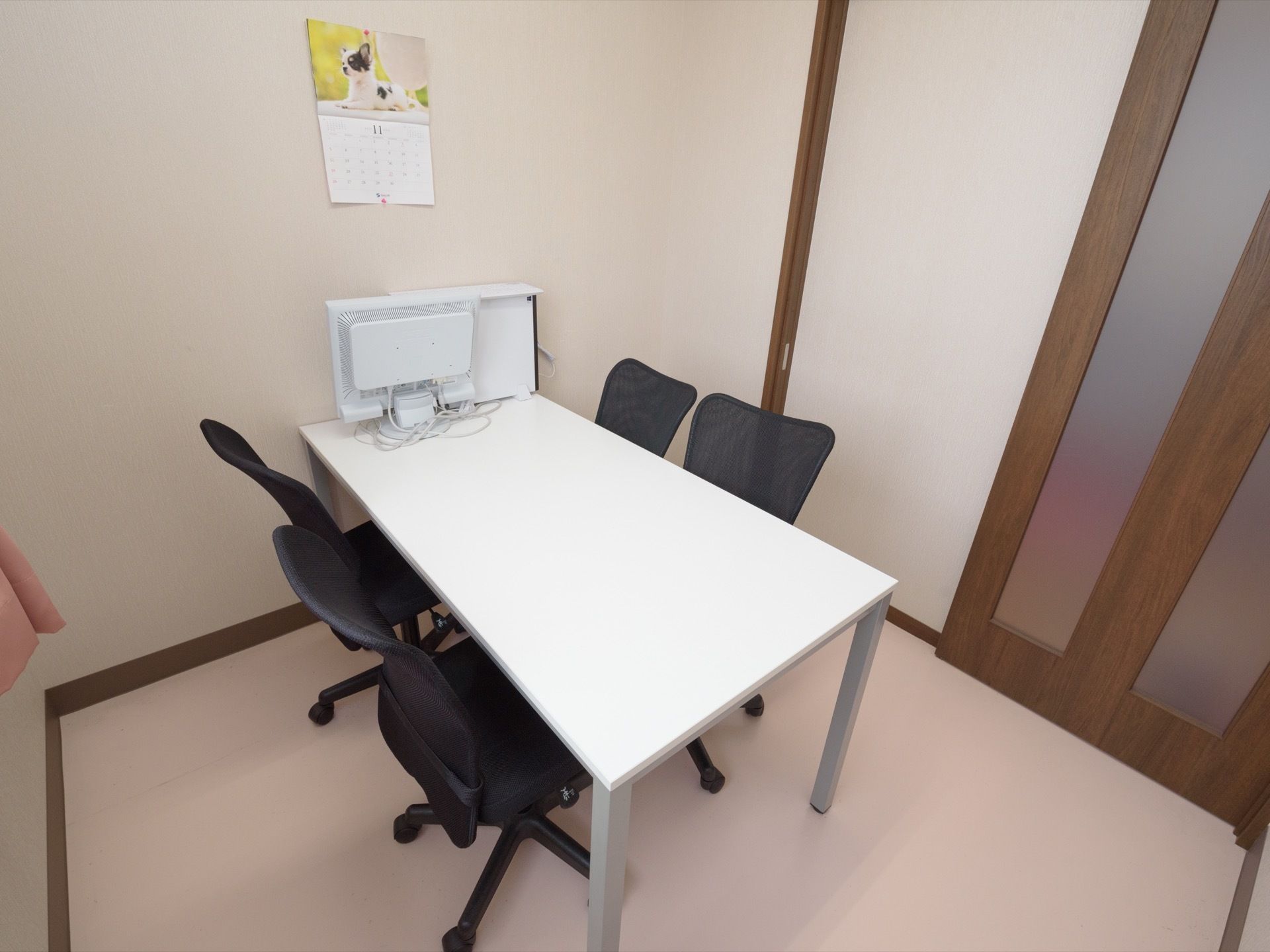 談話室は個室でテーブルが置かれイスが4脚備えられている。テーブルの上にはパソコンのモニターが置かれている。壁にはカレンダーが掛けられている。