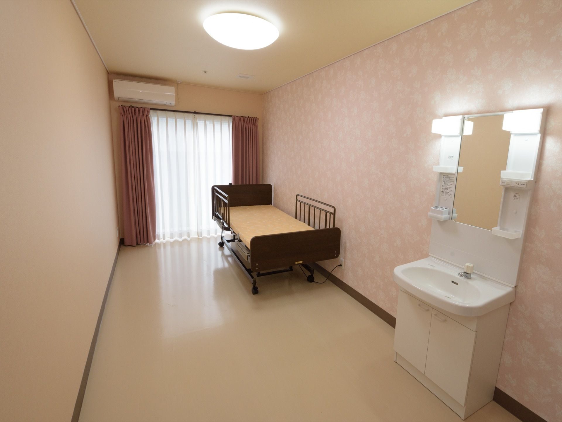 空調、電動ベッドに洗面化粧台を備えた居室。フロアは撥水する素材を使用しており、掃除をしやすい。電動ベッドには落下防止用の柵がある。