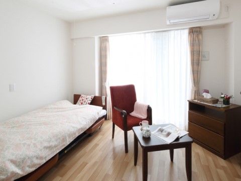 個室の居室である。ベッドやテレビ、テーブルなどが備えられている。大きな窓があり、カーテンが掛けられている。