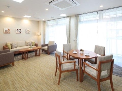 オフホワイトを中心に上品な色合いで統一された一室。木製のテーブルセットとソファセットが用意されている。窓は大きく、壁には絵画が飾られている。