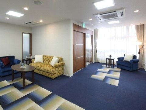 深い青のカーペットが敷かれ、ソファとテーブルが置かれたエントランス。大きな窓から光が入り、明るくくつろげる空間である。