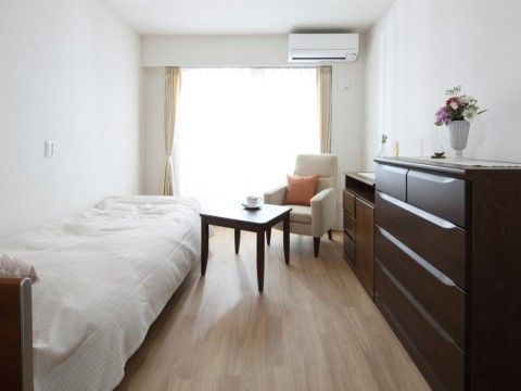 縦長のワンルームタイプで、エアコン付きの部屋である。収納家具を壁面に付けて置き、テーブルと椅子は中央に配置している。