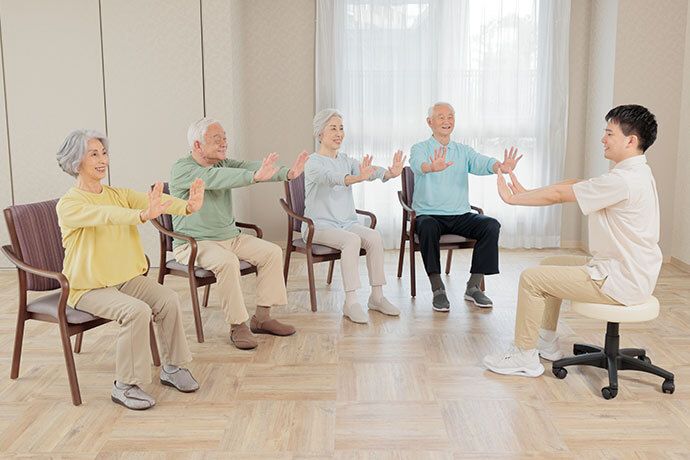 ピンク色の薄い布を両手に持って、椅子に座ったまま体操をする入居者様たち