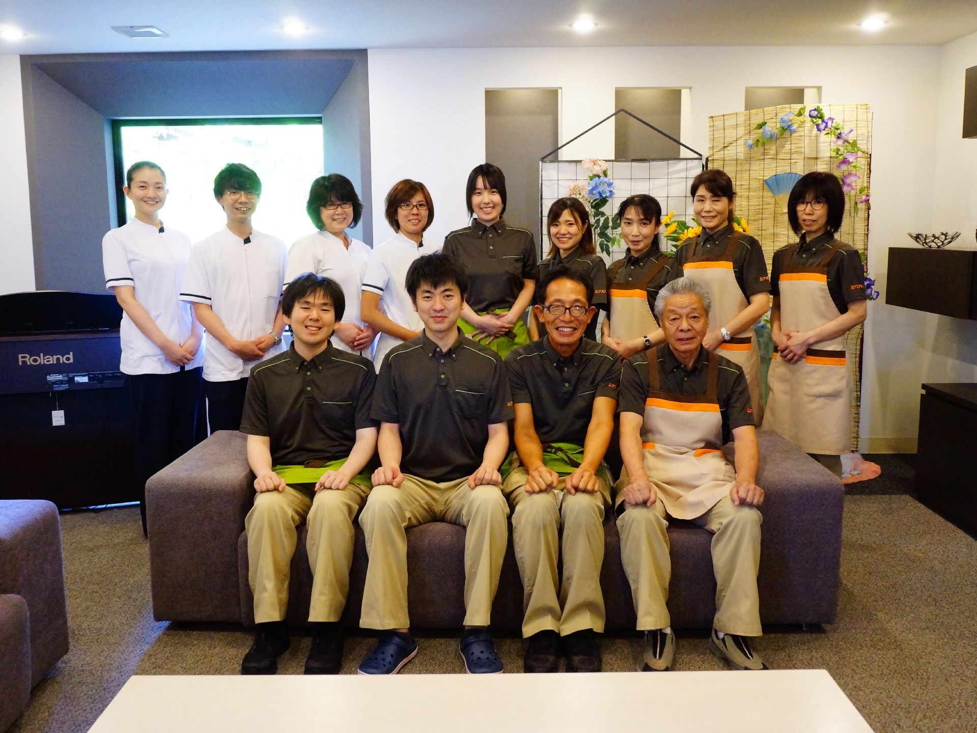 笑顔の女性スタッフと笑顔の男性スタッフが前後に分かれて写真に写っている。制服は担当によって違うものを身に着けている。