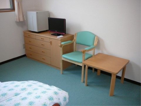 居室内には手すりが付いた介護用ベッド、椅子、テーブル、チェスト、テレビ、冷蔵庫が備え付けられている。
