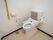 便器に背もたれと折り畳み式の手すりが設置されたトイレである。壁面には、手すりとケアコールが取り付けられている。