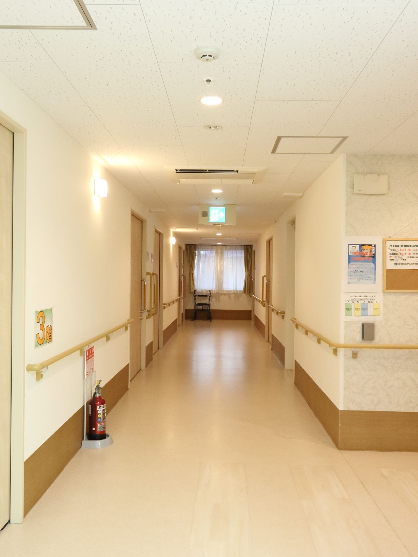 廊下の天井にはエアコンがあり、非常口への誘導灯が取り付けられている。また床には消化器が用意されている。