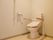 温水洗浄便座が付いた洋式トイレが設置されている。左右にはひじ掛けが追加され、壁には手すりやナースコールが取り付けられている。