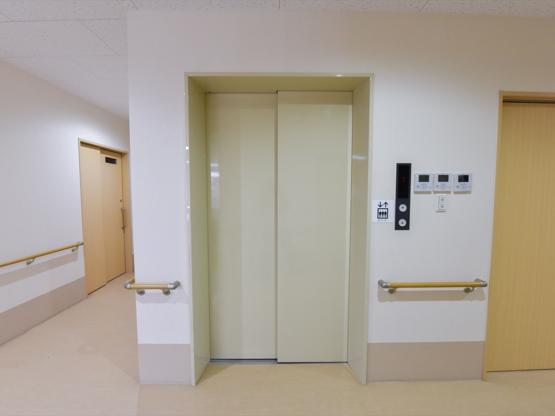 エレベーターまでの壁に手すりが設置してある。上下のシンブルなボタンの脇には、空調と電気の操作ボタンもある。