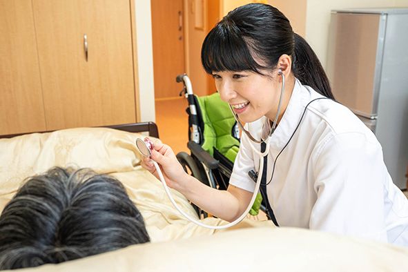 ベッドに横になっている入居者を、聴診器を使って笑顔で診察しようとしている白衣の女性