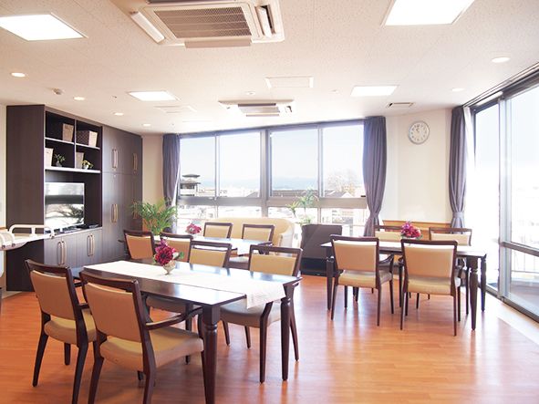 明るい室内に椅子とテービスが並んでいる。床はブラウン調の落ち着いた雰囲気である。