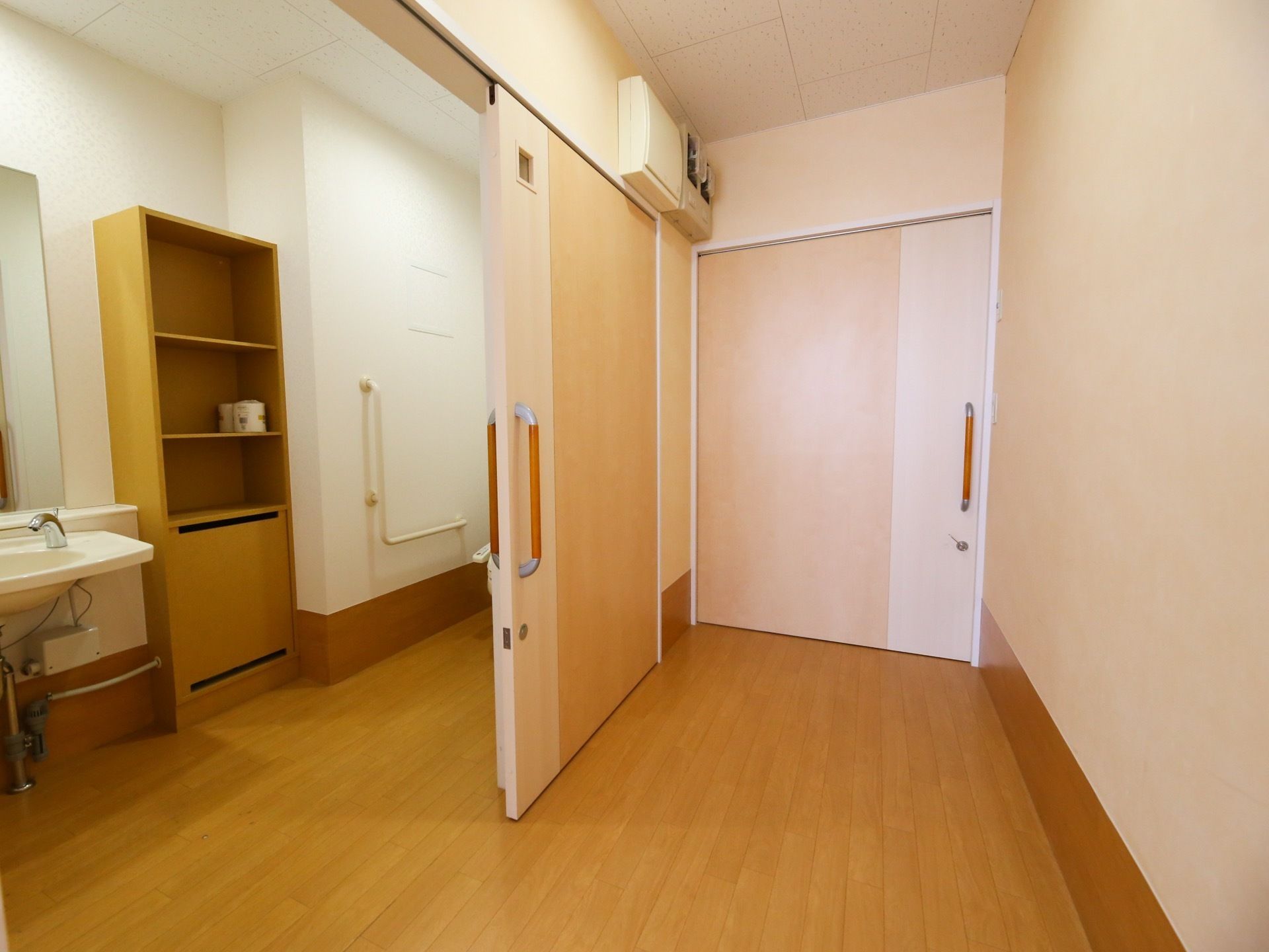 トイレのドアはスライド式で間口が広くなっている。ドアから少し入った奥に便座があり、Ｌ字の手すりが取り付けられている。