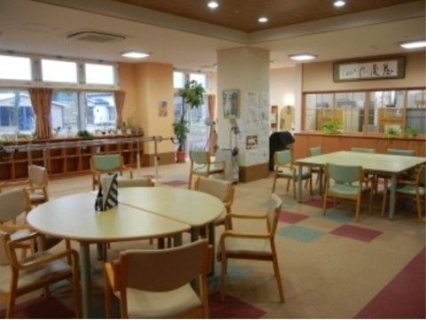 共用部には大きな窓があり、テーブル、手すり付きの椅子が置かれている。周囲には平行棒、観葉植物が置かれている。