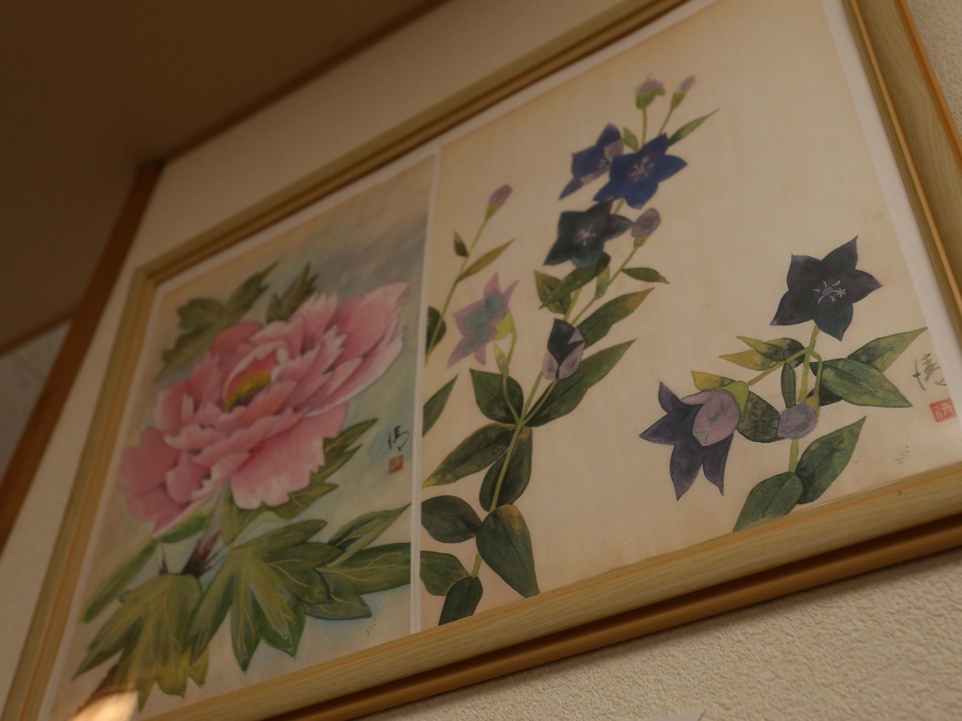 ボタンとリンドウの花を描いた日本画が額装され、壁に掛けてある。柔らかで落ち着いた雰囲気が感じられる。