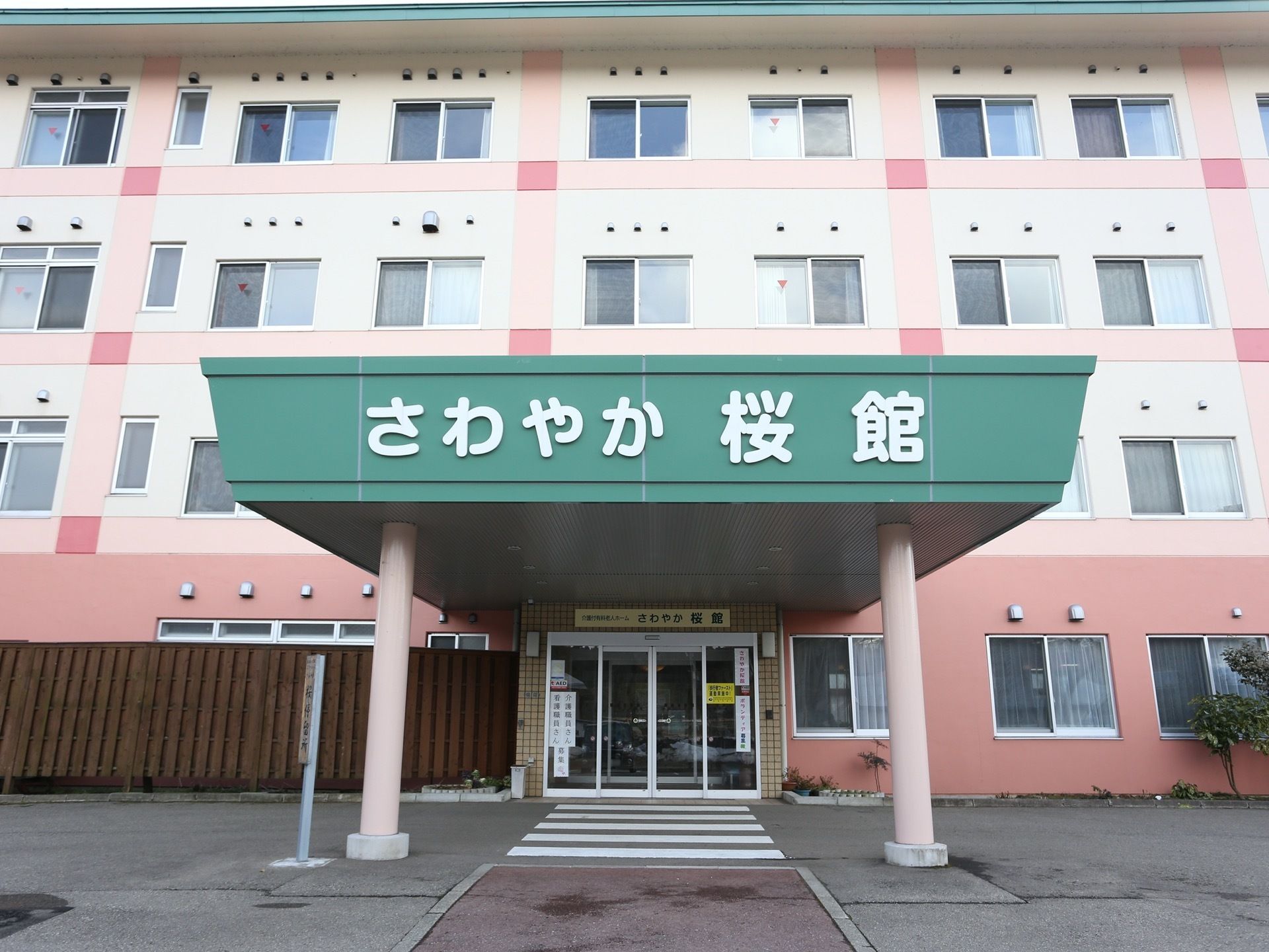 4階建ての大きな施設の外観は、名前の通り桜色でまとめられている。エントランスのひさしに、施設の名前が掲げられている。