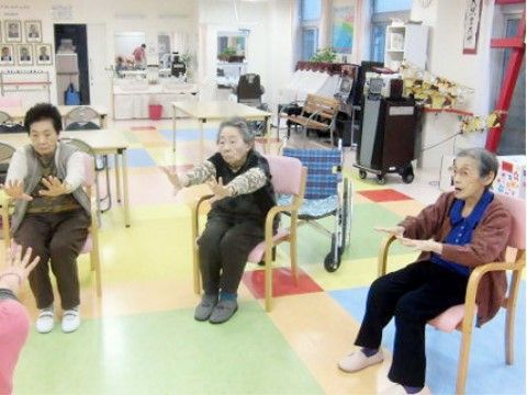 ピンク色の椅子に座って、両手を伸ばして体操をする三名の女性
