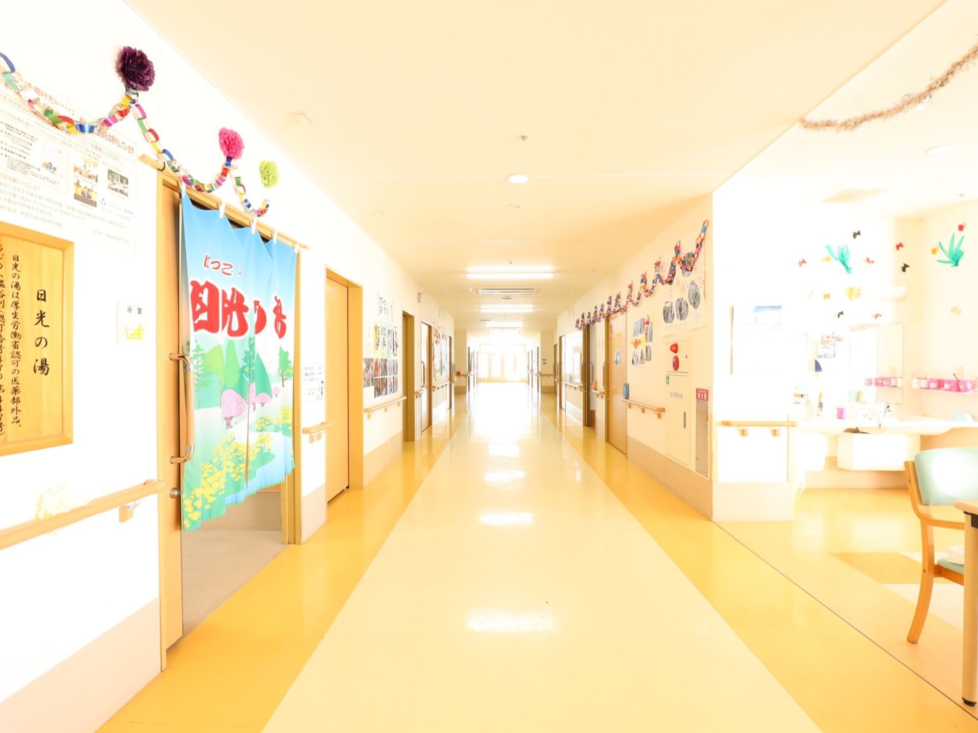 廊下の壁には手すりが設置されており、安全に移動することができる。突き当りの窓から外の光が差し込んでおり、明るい空間になっている。