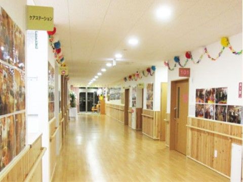 幅にゆとりのあるフローリングの通路。両側に手すりが完備され、障害物が何もなく安全である。壁には折り紙の飾りがあり、明るい雰囲気である。