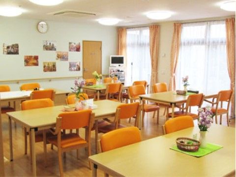 白とオレンジを基調とした明るいダイニングルーム。４人掛けのテーブルセットが並んでいる。壁には、写真が飾られている。