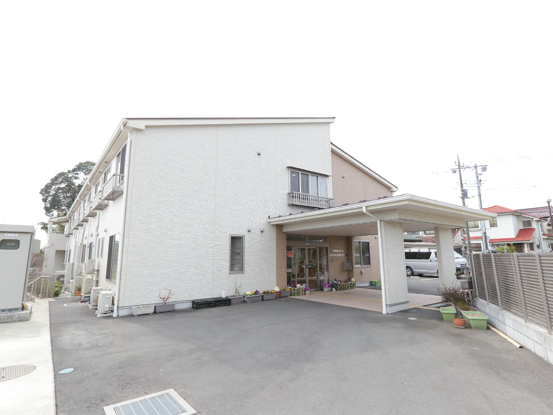 施設の壁は片側が白色、もう片側が茶色となっている。施設の周りには植木鉢に植えられた花などが置かれている。