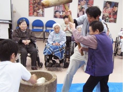 男性スタッフに補助されながら、餅つきをする女性入居者様