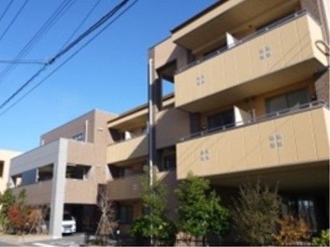 ブラウンを基調とした３階建てのグループホームである。２階以上にはベランダが設けられており、建前の前には複数の木が植えられている。