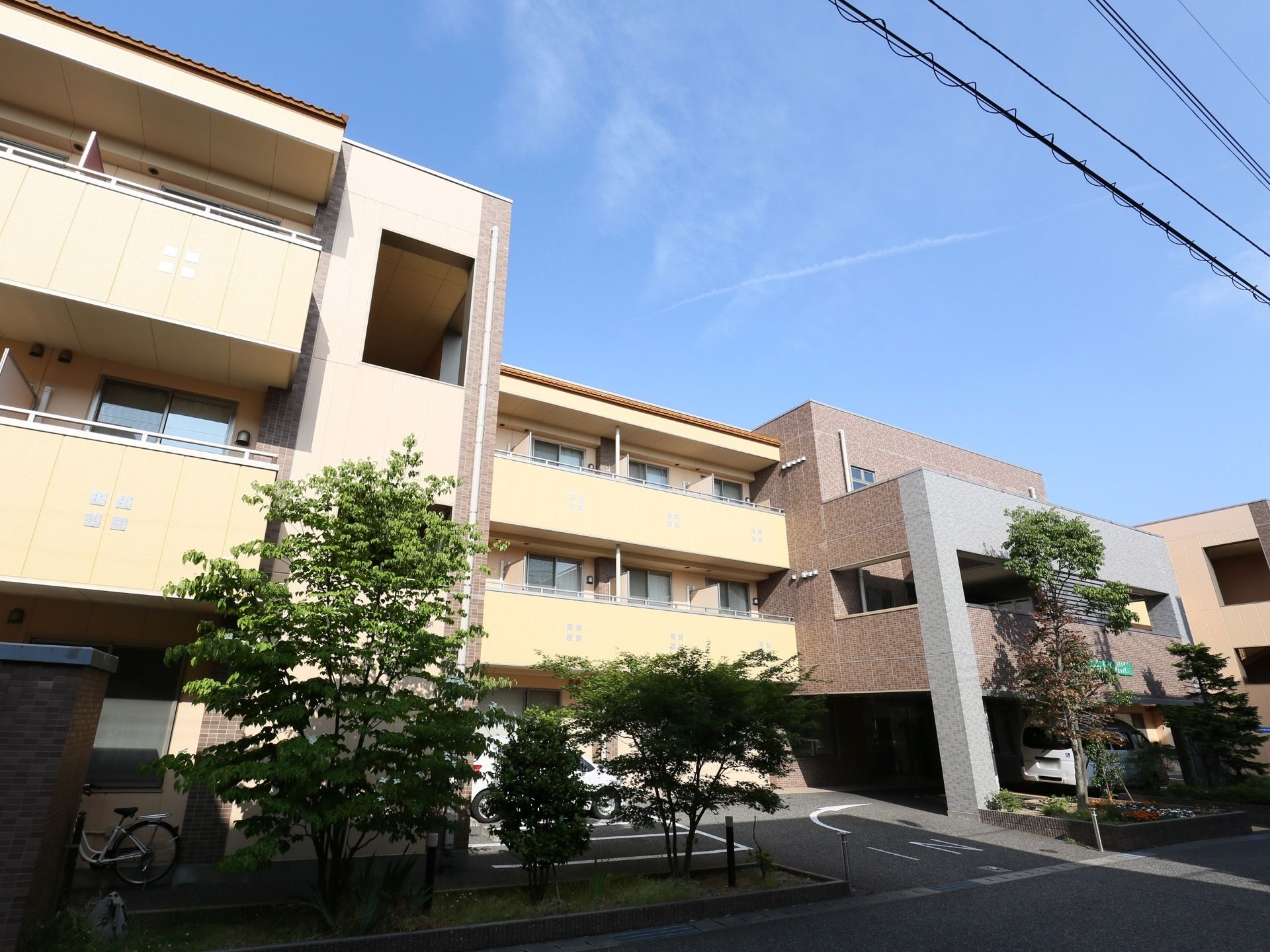 黄色と茶色を基調とした外壁の３階建ての施設である。玄関には車寄せがあり、道路からの進入路に入口を示す文字と矢印が描かれている。