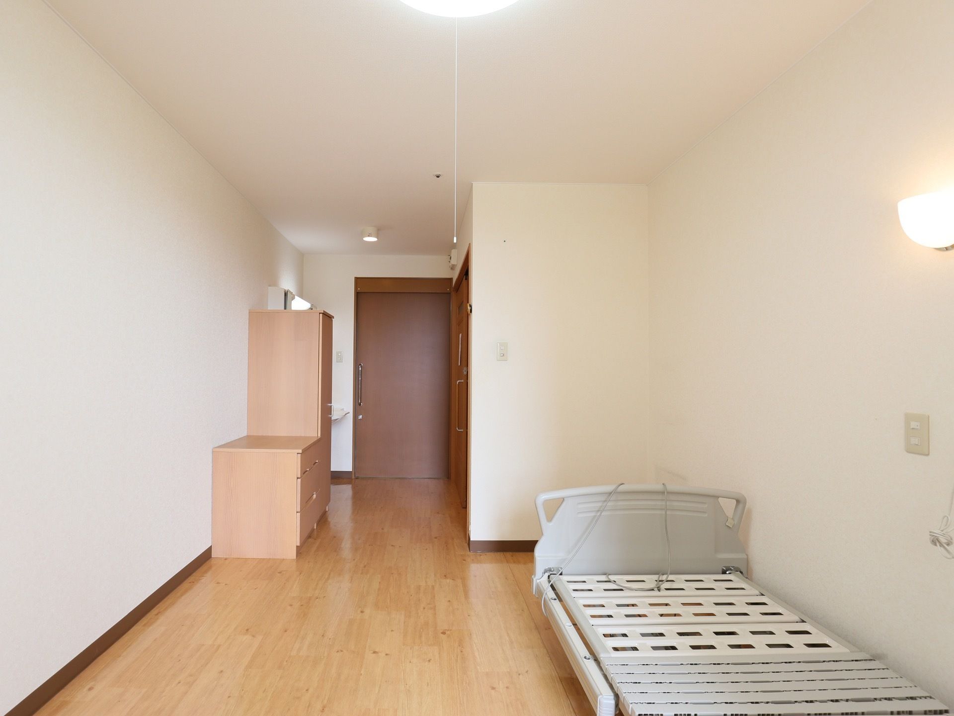 居室の入口は、取っ手がついた引き戸である。壁際に、高さの違う同色の収納家具が２つ並べて置かれている。