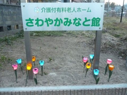 花壇に施設名が書かれた看板が設置されている。土にはチューリップをモチーフとした照明が複数設置されている。