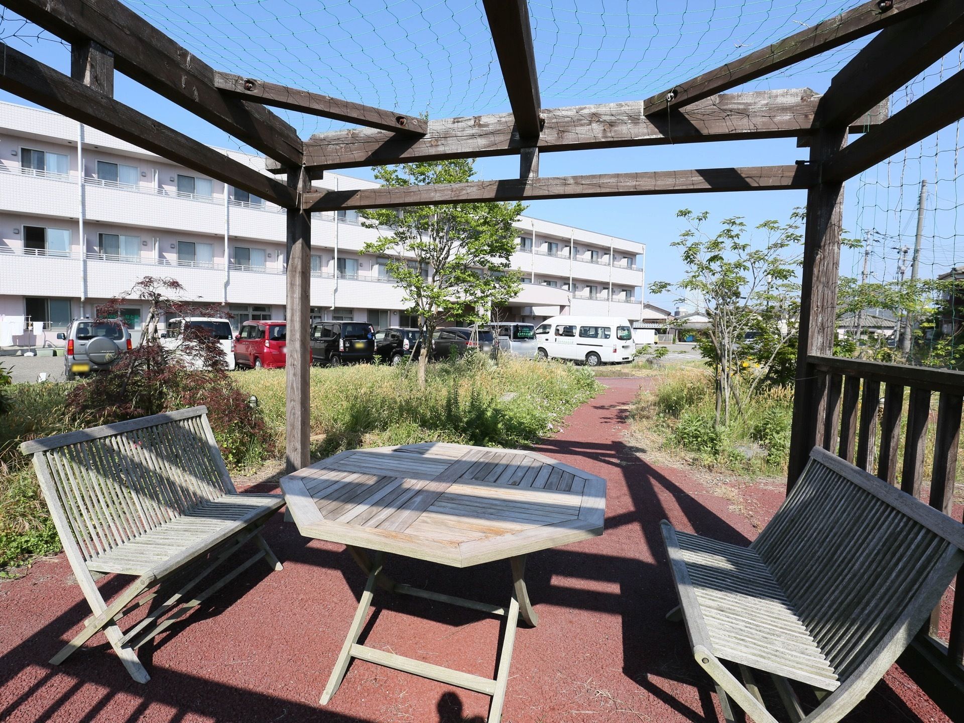 敷地内の植栽の間に、舗装された遊歩道がある。その途中に、木製のガーデンテーブルやベンチが置かれた休憩スペースが設けられている。