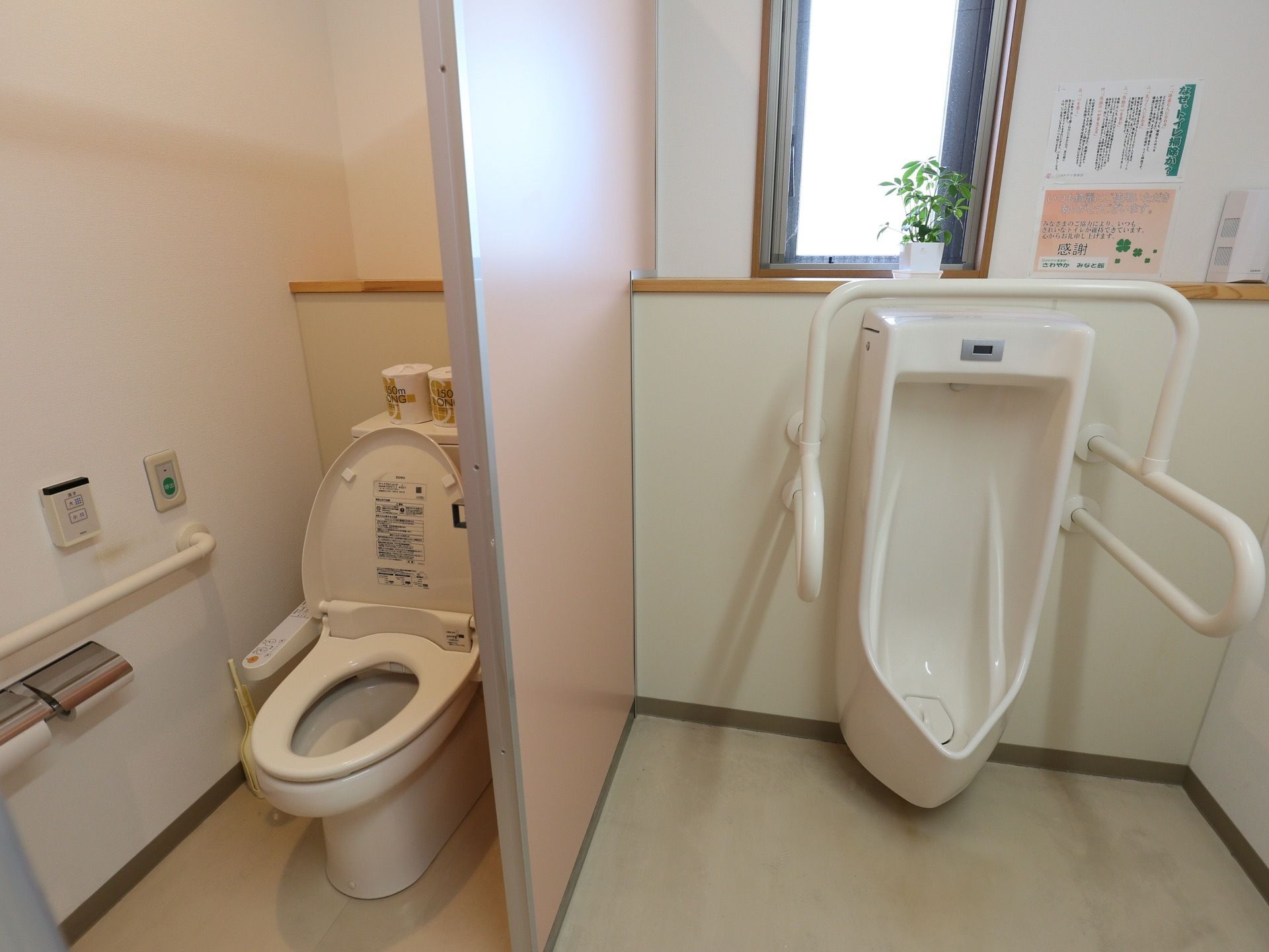 共同トイレには、男性用と男女共用の便器が並んでいる。その間には、ピンク色の仕切り板が設置されている。