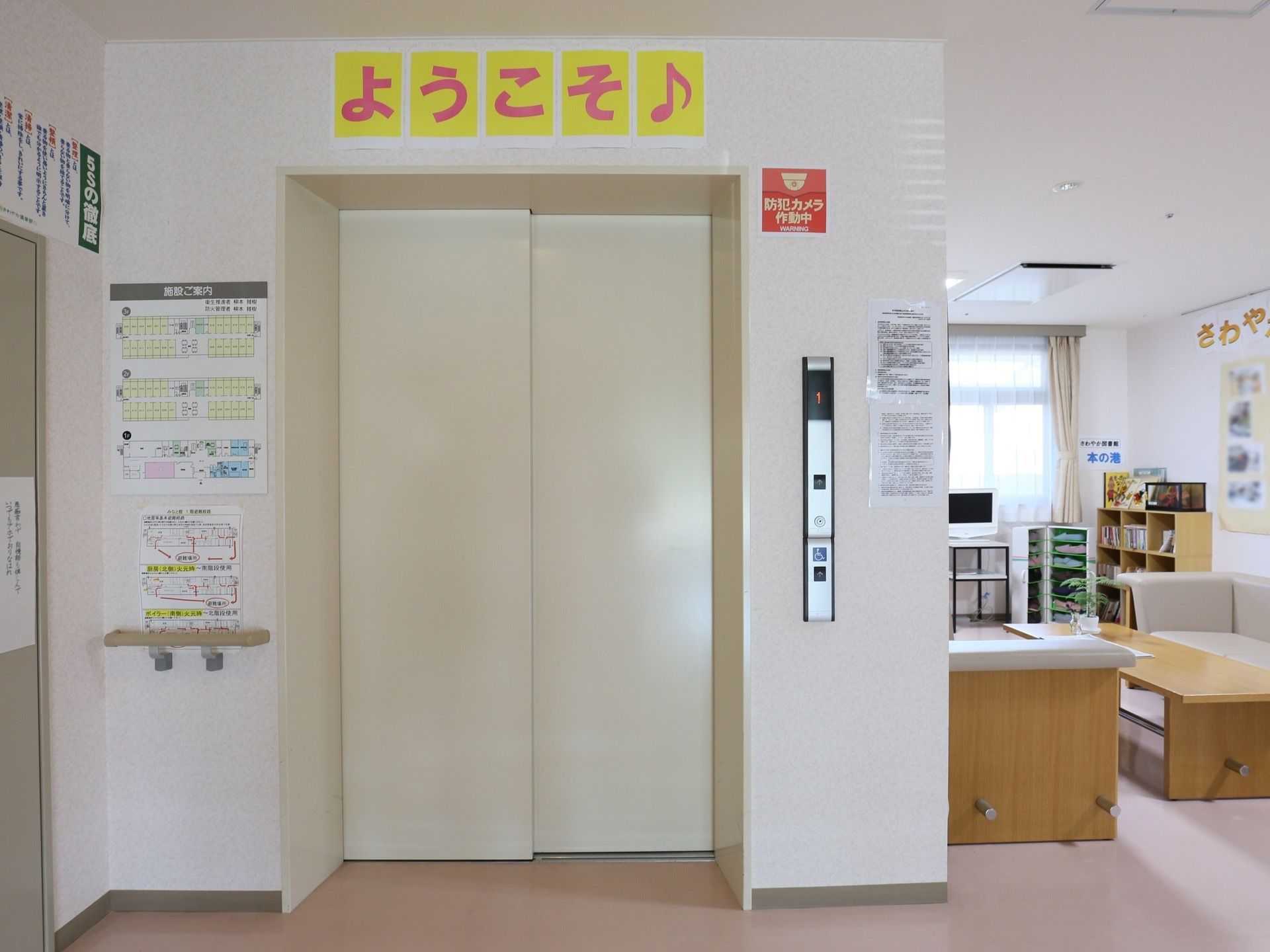 エレベーター乗降口の左側には、施設内の案内図が掲示されている。防犯カメラが作動していることを示すステッカーが貼られている。