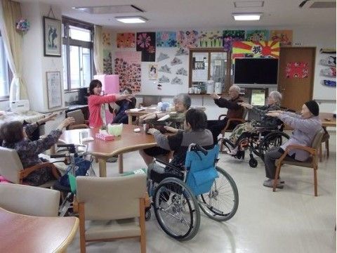女性スタッフを真似ながら、両腕を伸ばして体操をする入居者様たち