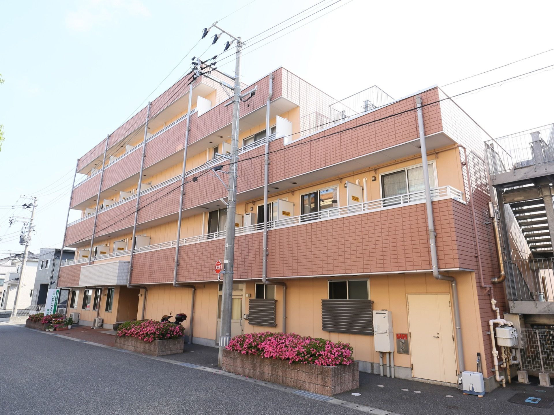 ４階建ての集合住宅のような外観の建物には、エントランス周辺に花壇が設置され色鮮やかな花が咲き誇っている。