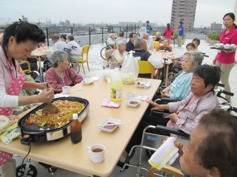 屋上に設置されたテーブルで、焼きそばを焼いているスタッフを眺めている入居者様