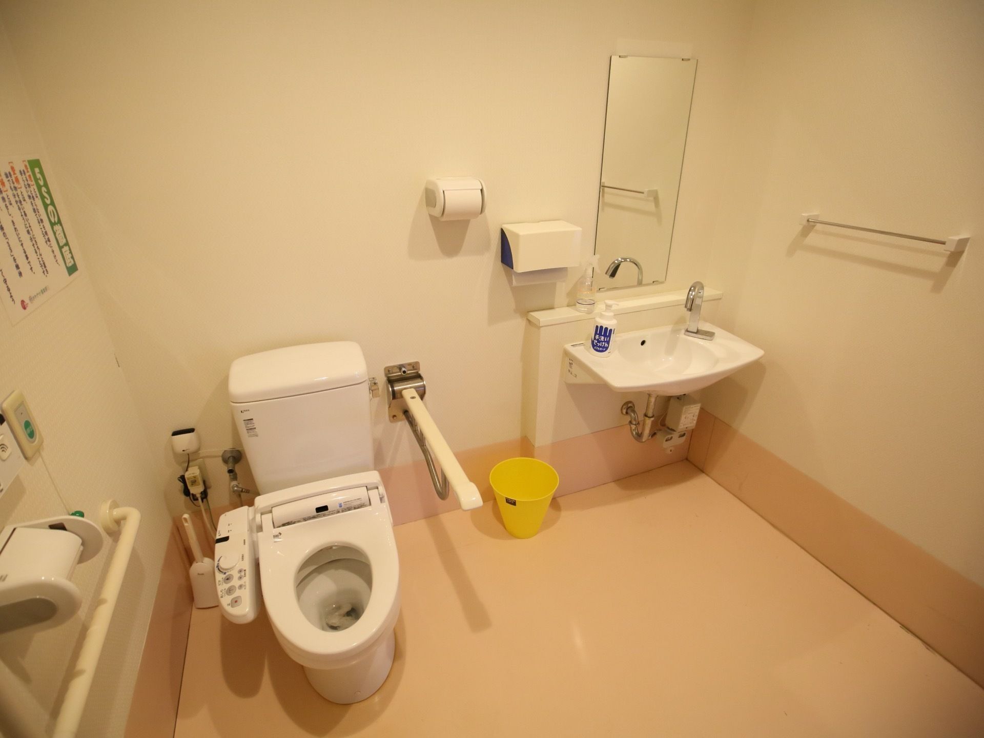 広いスペースのある共用トイレが設置されている。自動水栓がついた洗面台が便器の右側に取り付けられている。