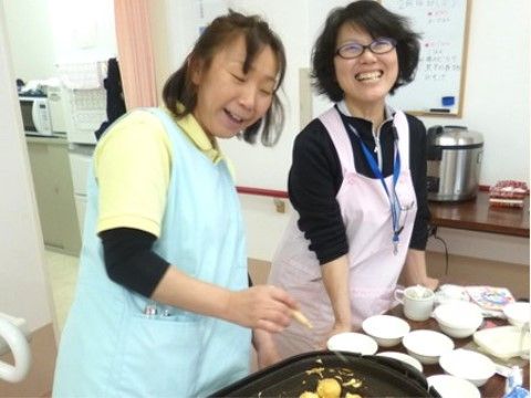 笑顔でたこ焼きを焼いている、エプロンを着用した二名の女性スタッフ