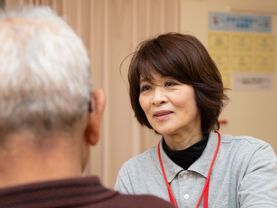 女性のスタッフが、男性の入居者様と笑顔で会話している。24時間体制で入居者様の生活のサポートを行っている。