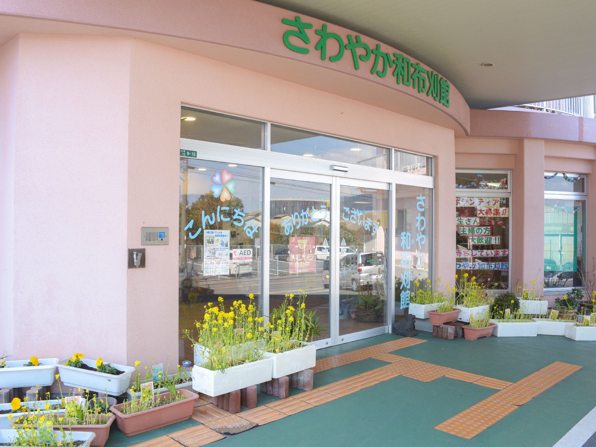 ガラス張りの自動ドアの前には、たくさんの草花が植えてある。レンガ色の壁には、黄緑色の大きな文字で施設名が書かれている。