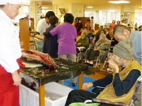 コック姿の男性がマグロを解体した場所の近くにいる、車椅子の男性入居者様