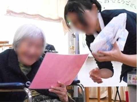 スタッフに見守られながら、手にピンク色の歌詞カードを持って歌う入居者様