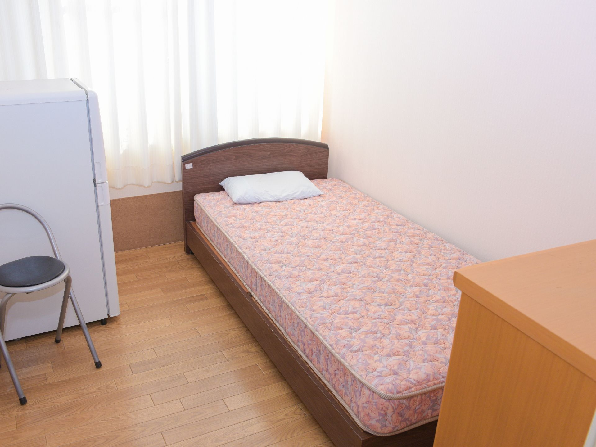 大きな窓があり、冷蔵庫やパイプ椅子、マットレスが使われた普通のベッドが置かれた居室。レースカーテンを通した柔らかい日差しが差し込んでいる。