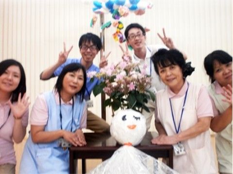 花や大きなてるてる坊主の周りに集まり、ポーズをとっているスタッフたち