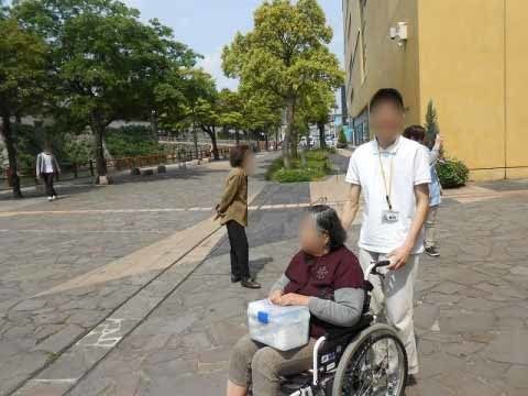 男性スタッフに車椅子を押してもらいながら、散歩をする入居者の女性