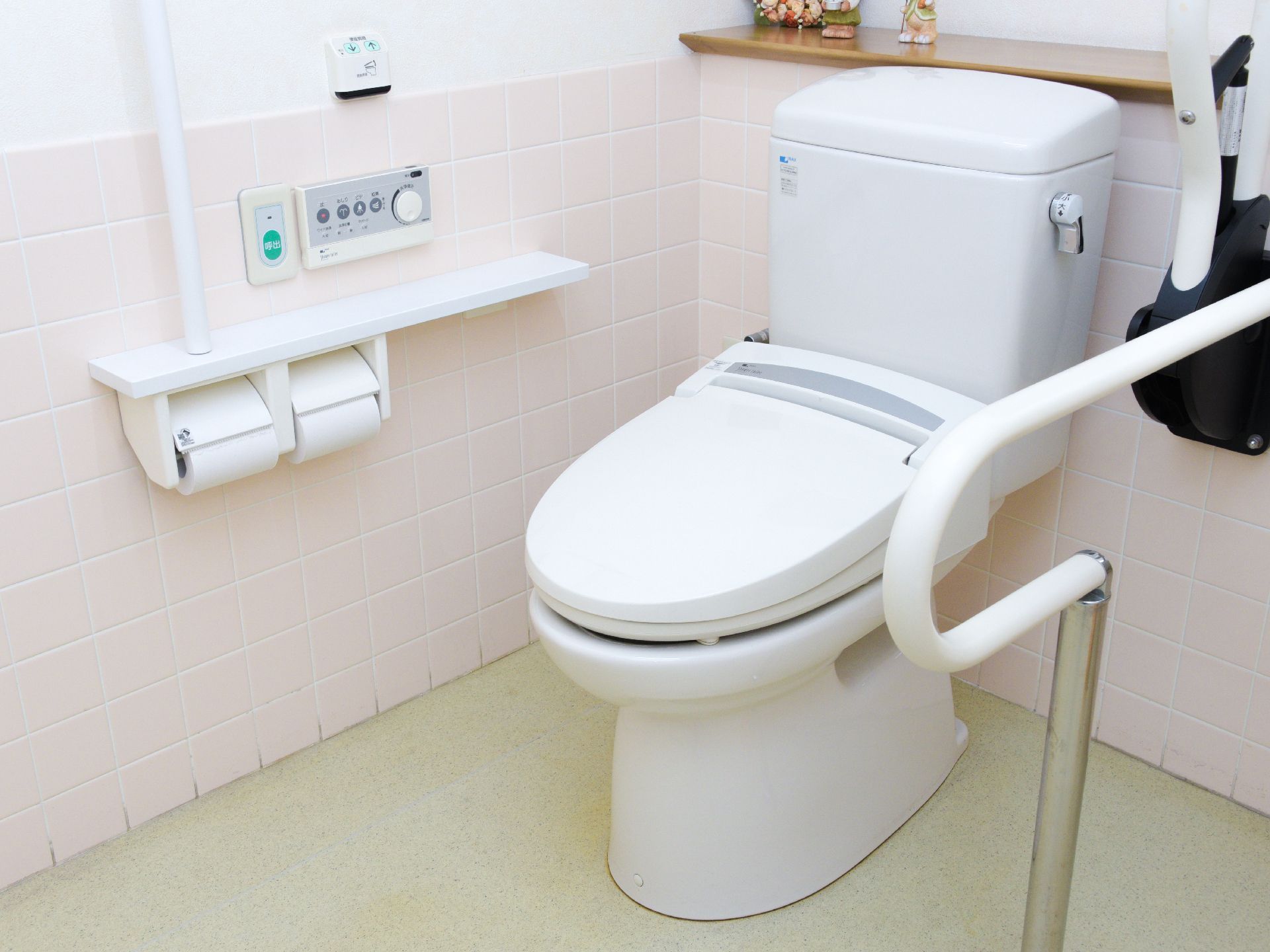 便器の両側に手すりがついたトイレ。一方は壁に、もう一方は可動式の手すりがついている。緊急時の呼び出しボタンもついている。