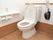 トイレは広々として清潔感があり、壁の色はベージュと白の2色である。棚、コンセント、緊急呼出ボタン、手摺が設置されている。