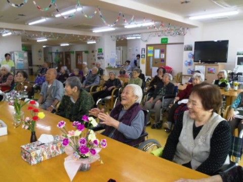 花瓶がいくつも飾られたテーブルの前で、笑顔で座っている入居者様たち