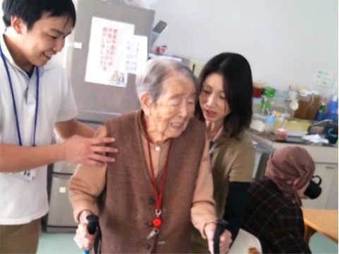 スタッフたちに支えられながら、両手に持った杖を使って歩く女性