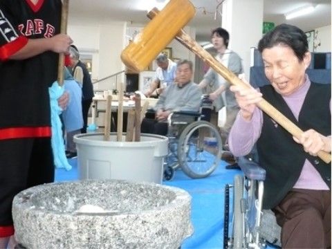 自分自身で杵を持ちながら、車椅子に座って笑顔で餅つきをする女性